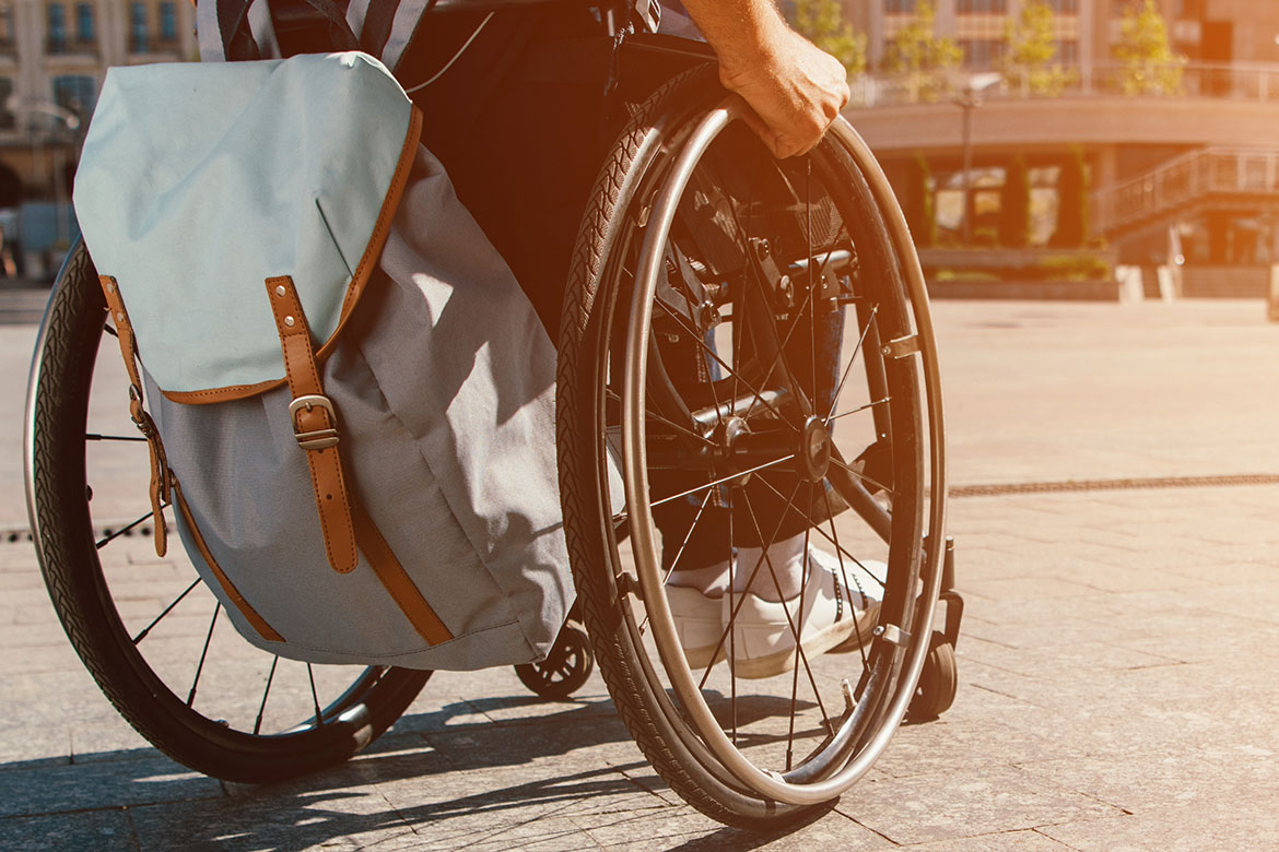 cropped panoramic view of man using wheelchair with bag on stree